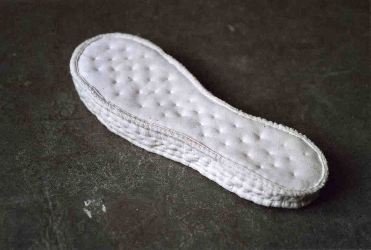 Semelle en tissu évoquant un matelas molletonné en forme de semelle, face recto.