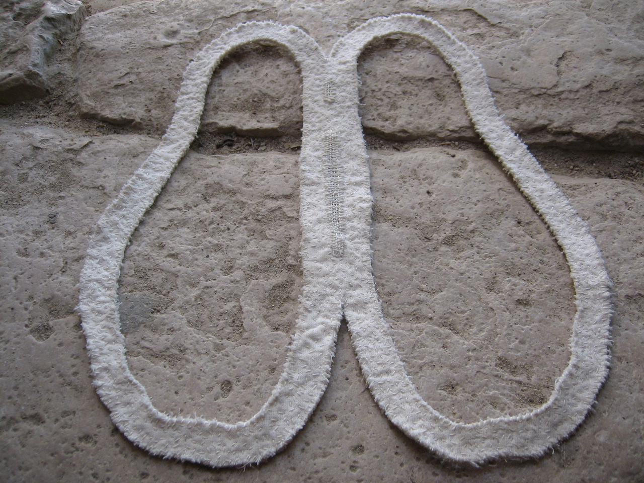 Contour de deux pieds posés au sol, en tissu blanc sur-brodé.
