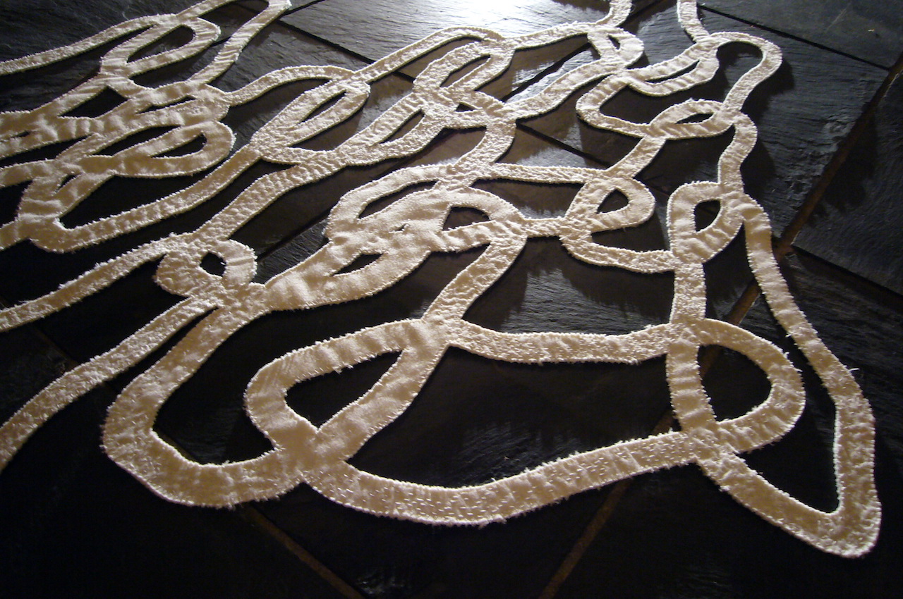 Détail d'une île de contours de pas entremêlés en tissu blanc sur-brodé.