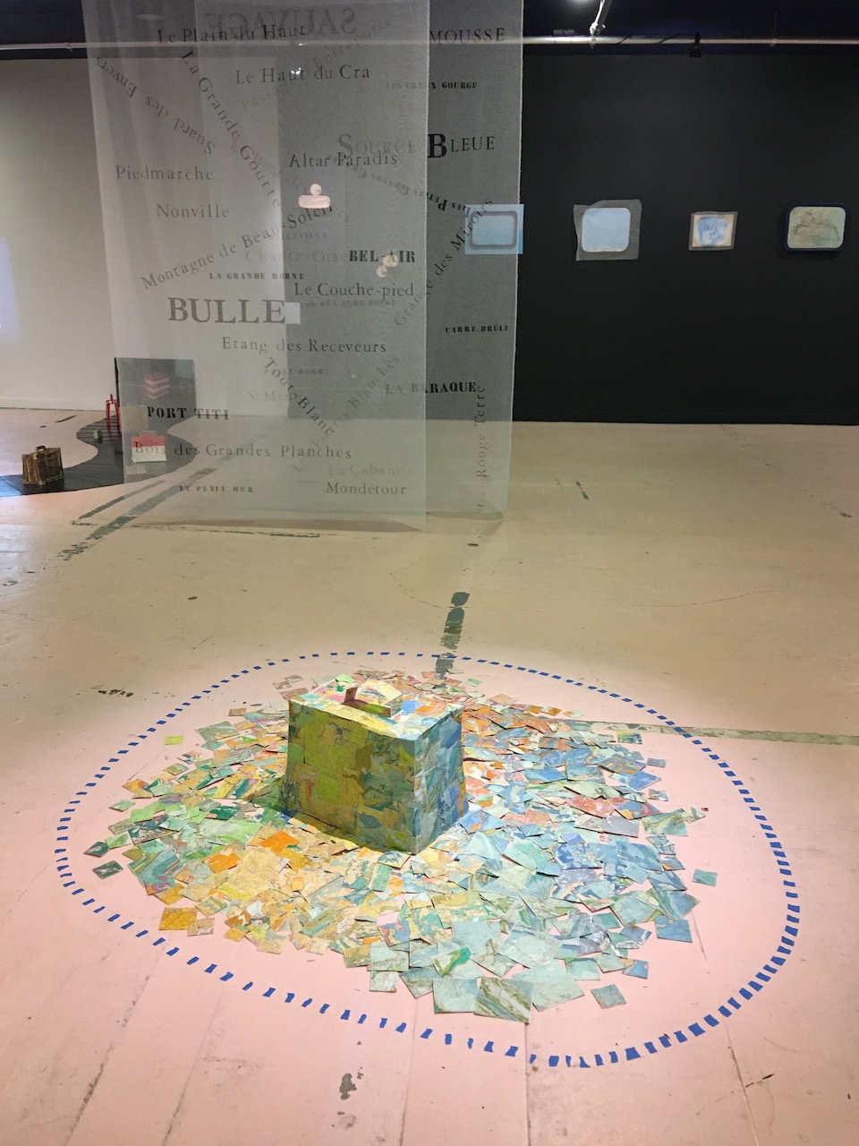 Vue de l'exposition avec une valise-île en premier plan et des tissus translucides au fond