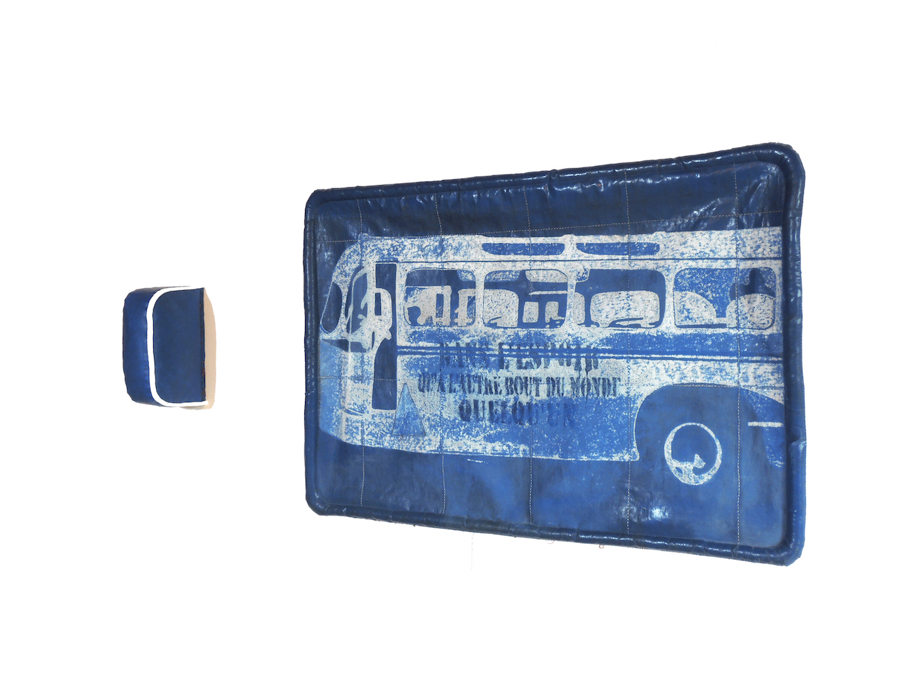 Objet mural comportant un coussinet de tête et une fenêtre en bâche de camion bleue par laquelle on voit un bus sur lequel il est écrit Dans l'espoir qu'à l'autre bout du monde quelqu'un. Le dessin est frotté dans la bâche pour laisser apparaître la trame blanche intérieure.
