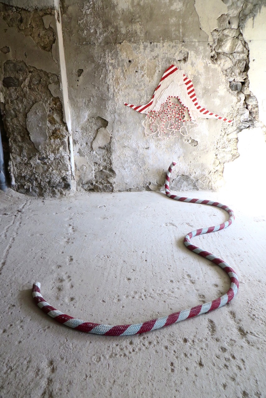 Vue d'une pièce textile accrochée au mur avec une corde au sol, le tout évoque la frontière
