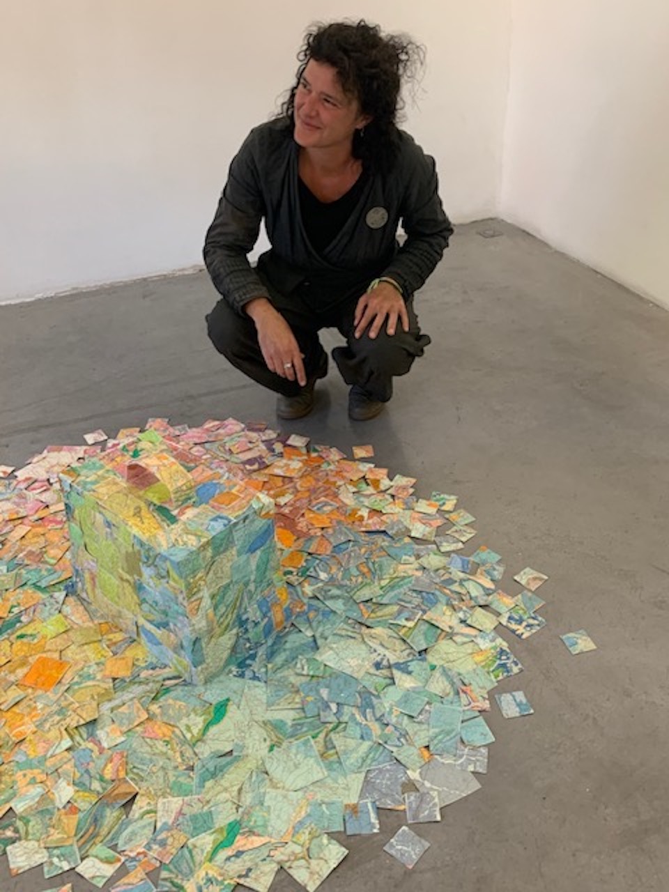 L'artiste au pied de la sculpture d'une valise-île faite en cartes géologiques très colorées