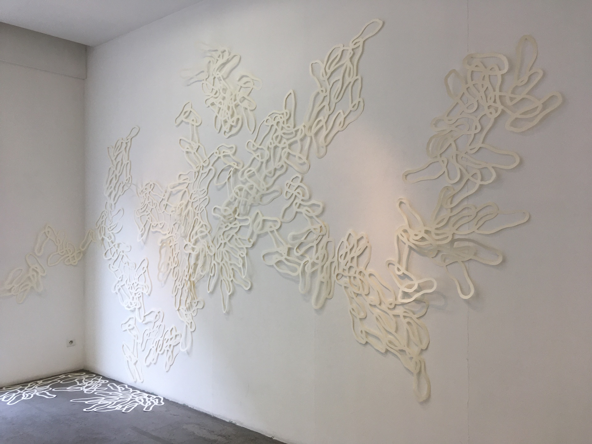 Installation murale d'une accumulation d'île de pas découpées dans des feuilles de papier simili japon, clouées au mur et déposées au sol