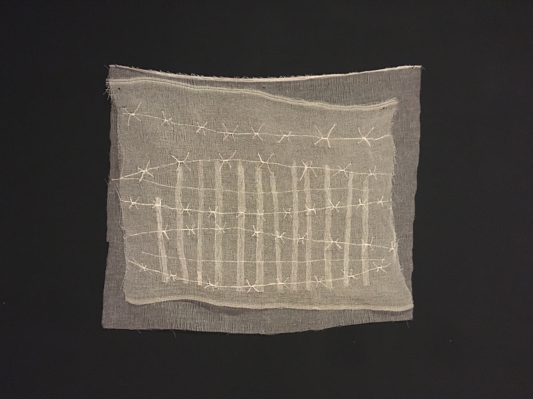 2 couches de matériaux blancs translucides (tarlatane et grillage) qui sont brodés au fil blancs avec une barrière et une série de fil barbelés