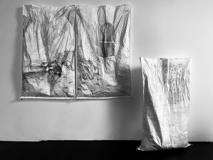 Dessin au graphite sur 3 sacs à gravats blancs d'un abri de fortune devant des publicités pour les jeux olympiques de Paris