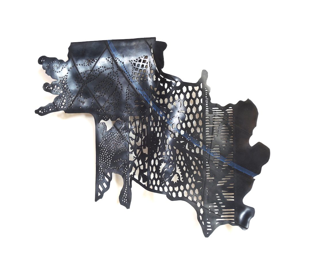 Objet mural en chambre à air ajourée monté sur une structure en aluminium. La forme évoque un fragment d'habit ou une carte géographique.