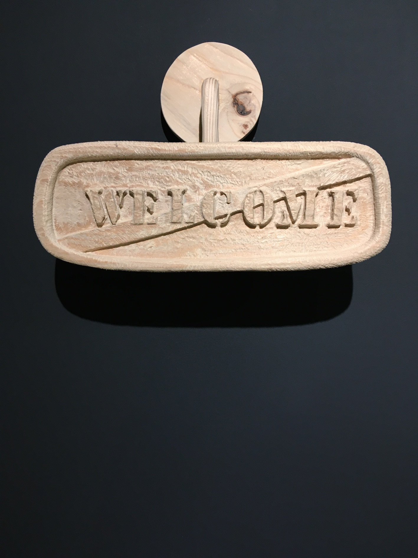 Rétroviseur sculpté dans du bois dans lequel on peut lire le mot Welcome barré comme à la sortie d'un village nommé Welcome.